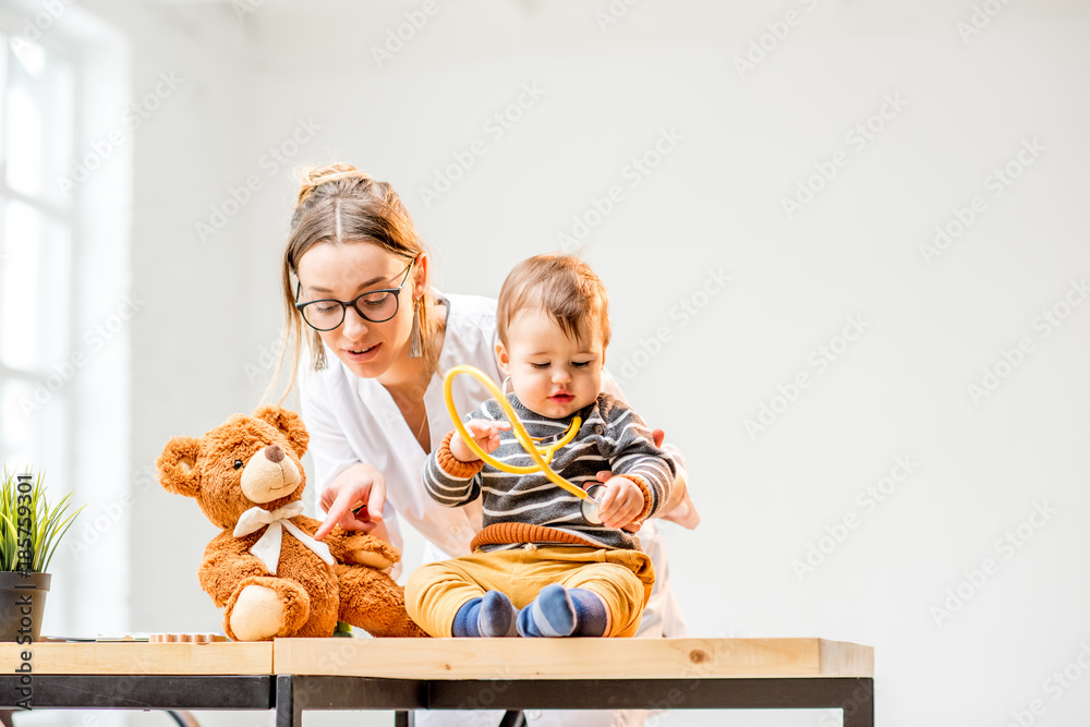 坐在办公室桌子上照顾男婴的年轻女儿科医生