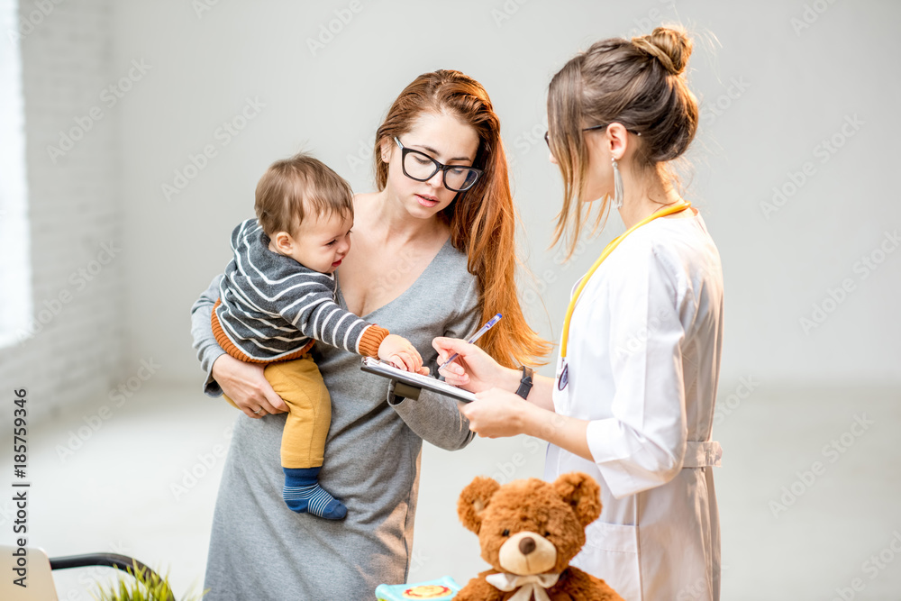 Mother with her baby boy during the consultation with young woman pediatrician standing in the white