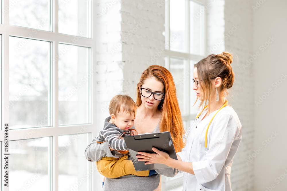 Mother with her baby boy during the consultation with young woman pediatrician standing in the white