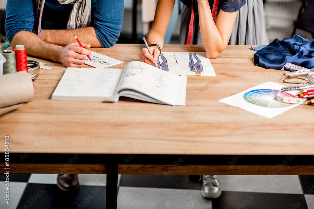 Couple of fashion designers drawing clothing sketches on the table. Close-up view on the table with 