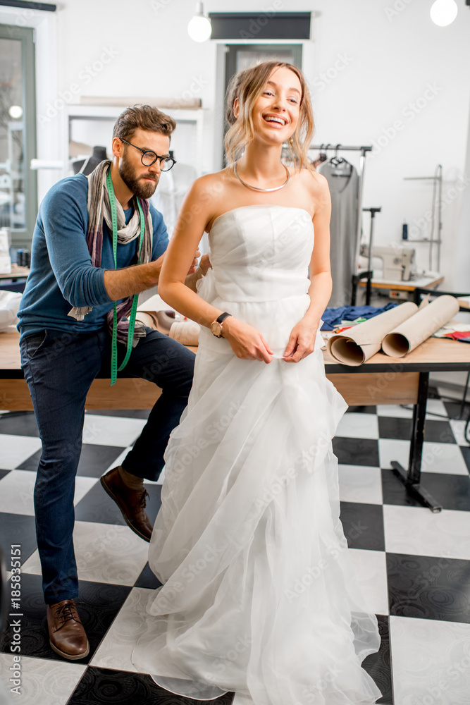 Young woman client fitting wedding dress with man tailor standing at the sewing studio