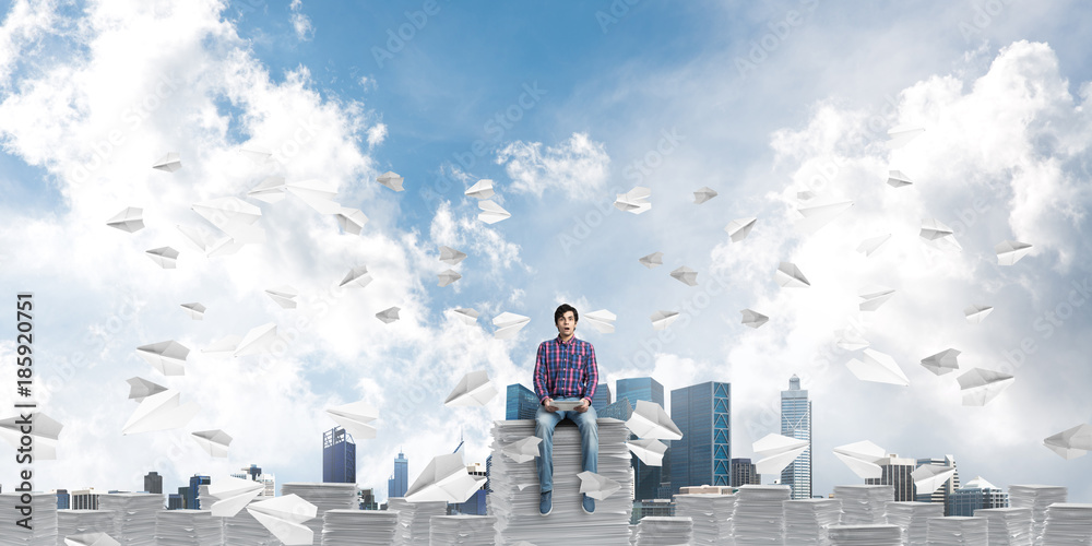 Attractive man sitting on pile of paper documents.