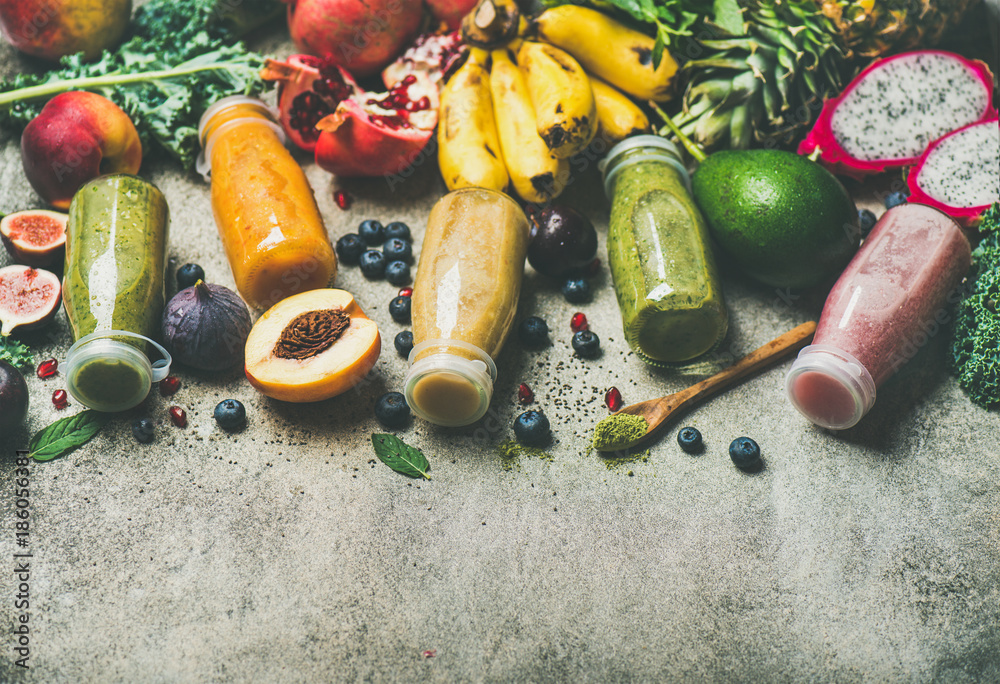 Colorful smoothies in bottles with fresh tropical fruit and superfoods on concrete background, selec