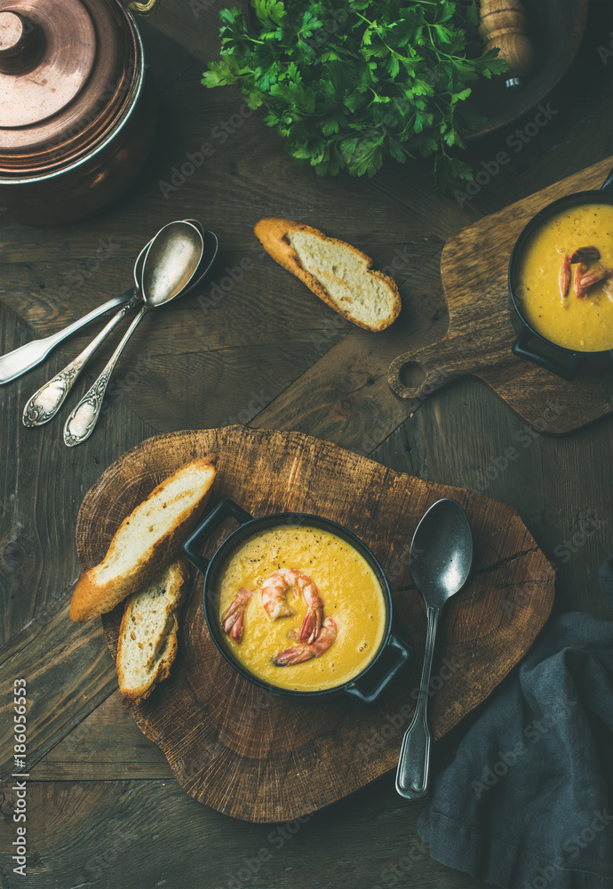 Flat-lay of corn creamy soup with shrimps served in individual pots with bread over rustic dinner ta