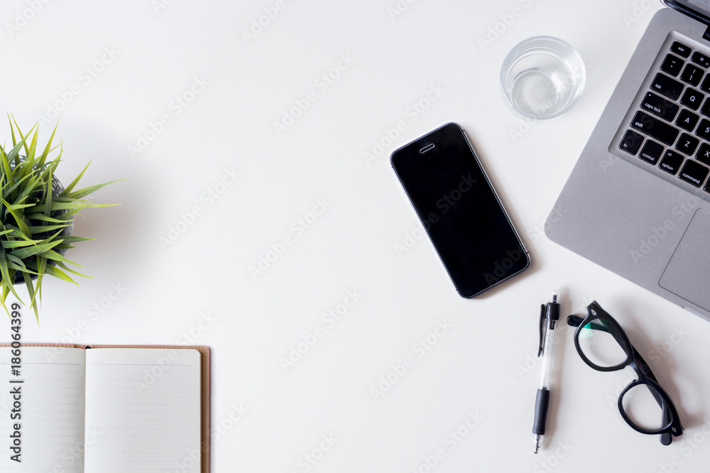 White office desk table with laptop, smartphone, notebook, and glass. Top view with copy space, flat