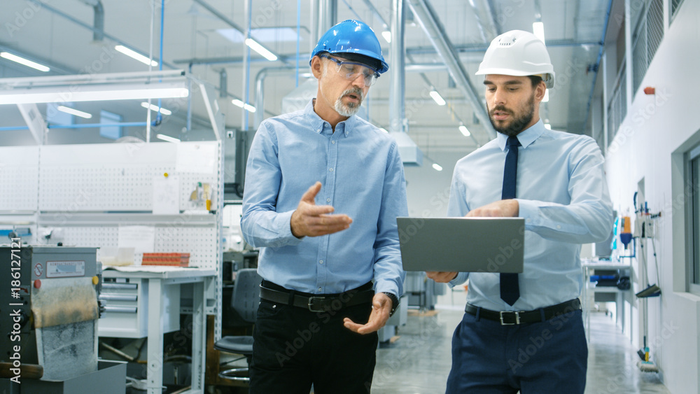 Head of the Department Holds Laptop and Discuss Product Details with Chief Engineer while They Walk 