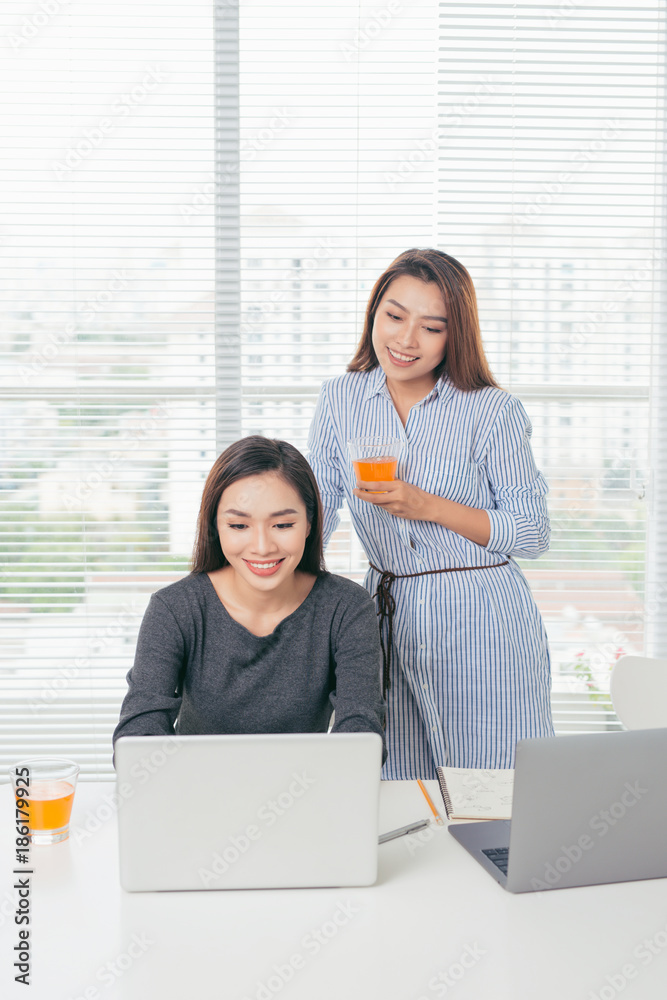 两位面带微笑的亚洲女商人在办公室里拿着笔记本电脑工作