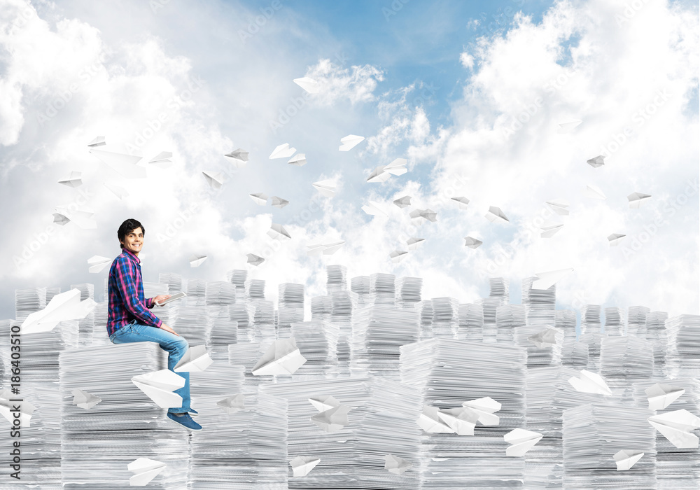 Attractive man sitting on pile of paper documents.