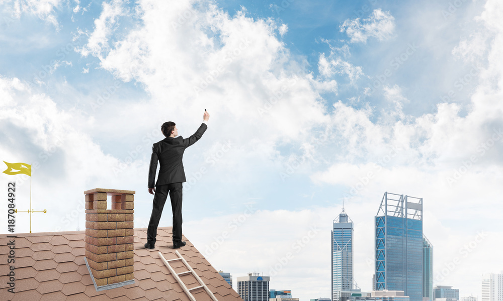 Businessman on house roof touch empty space. Mixed media