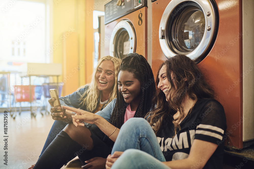 Friends using a cellphone on the floor of a laundromat