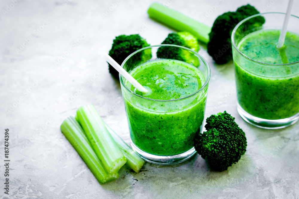 Green vegetable smoothie in glass at gray background