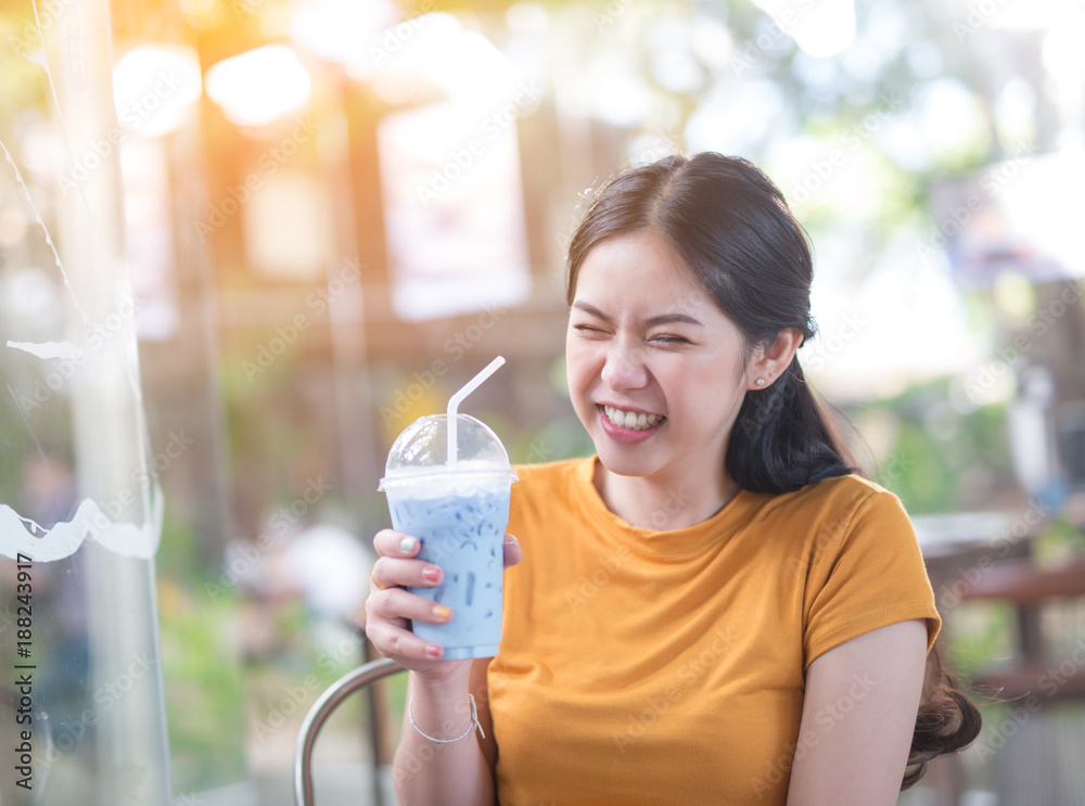 年轻快乐的亚洲女人在咖啡店笑着喝冰牛奶