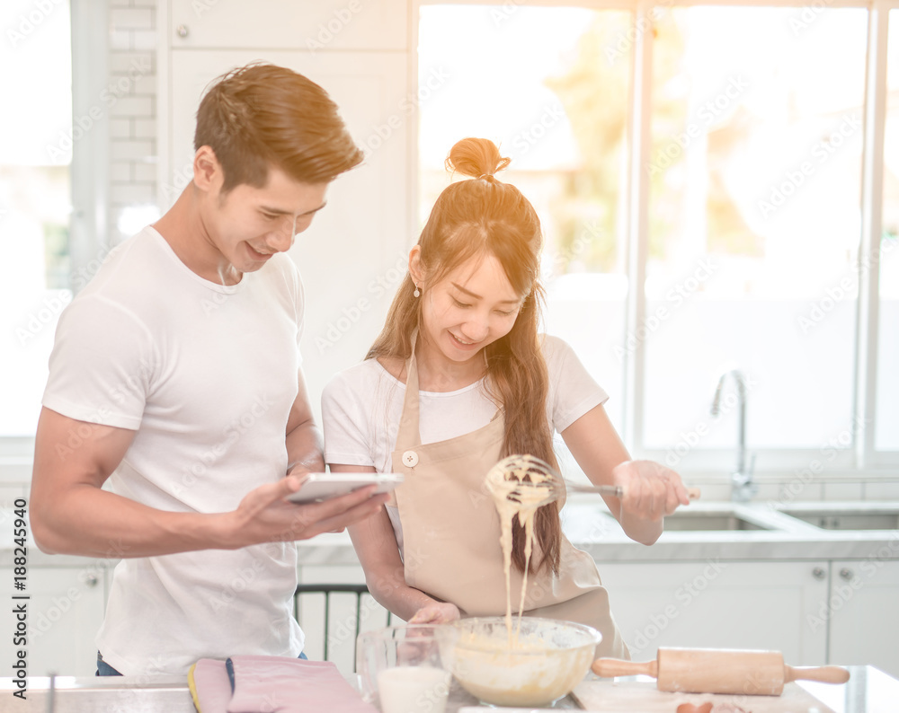 一对年轻的亚洲夫妇高兴地让面包师帮助制作面包店——从平板电脑上看到食谱