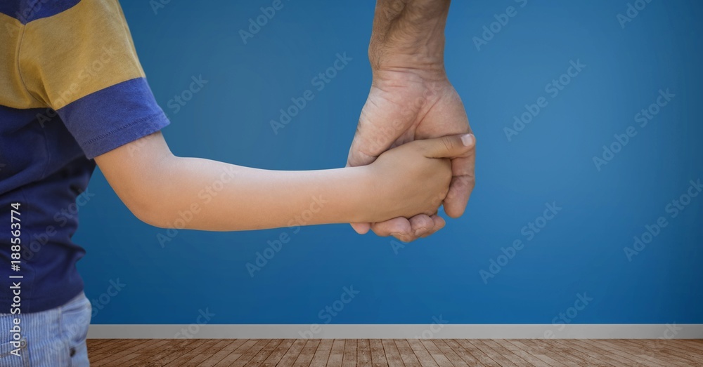 Child holding adults hand with blue wall in room