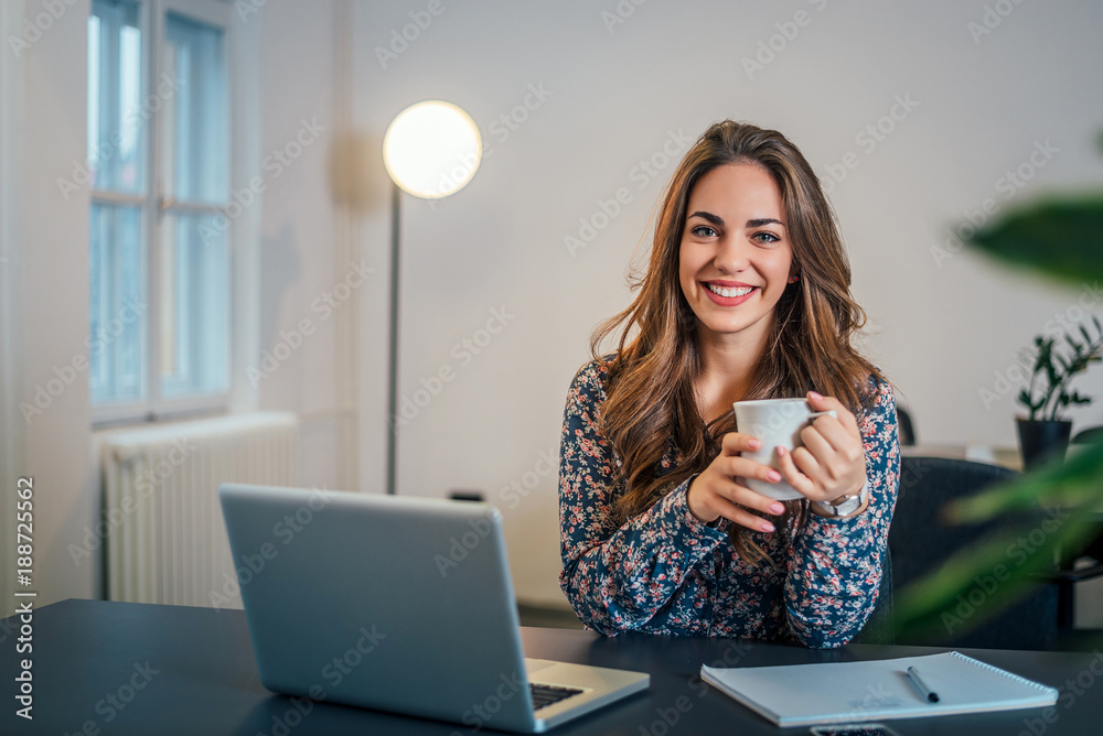 Portrait of attractive woman in office holding cup of coffee.