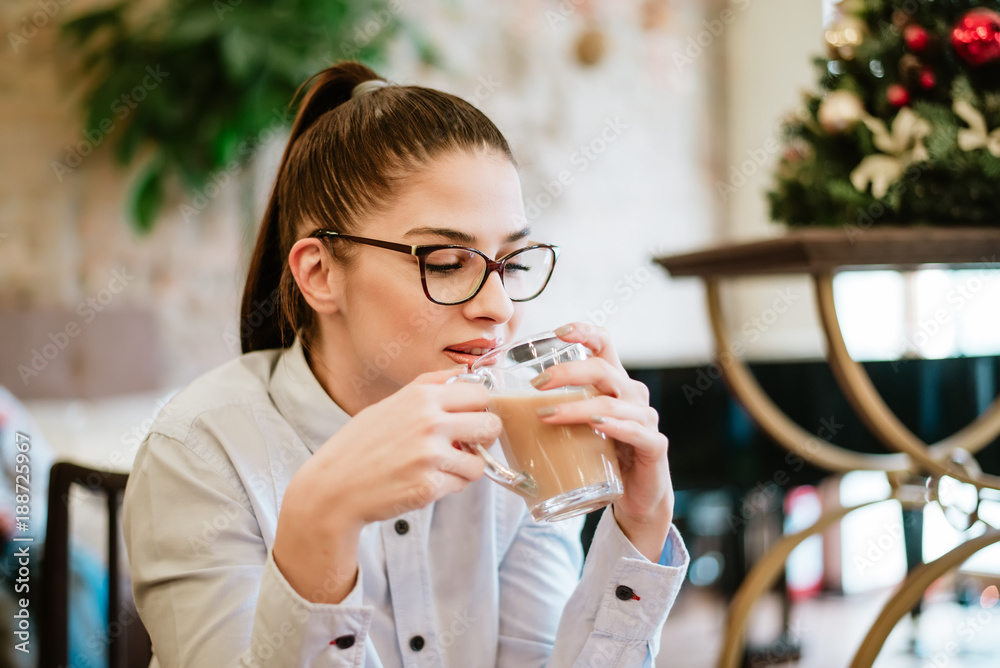 Young beautiful girl with eyeglasses enjoying coffee at cafe.