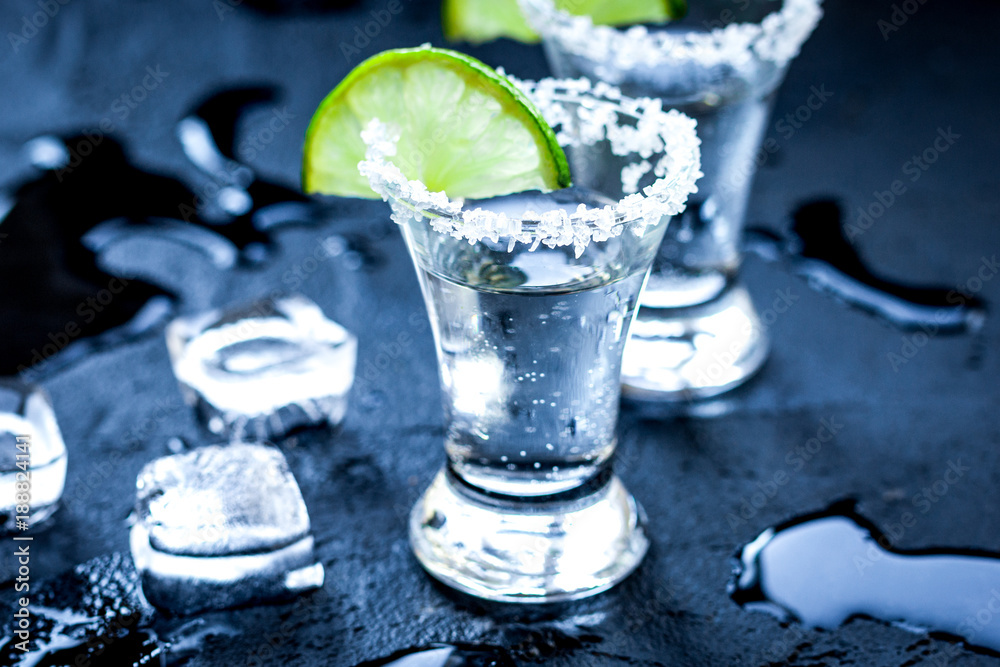 Silver tequila shots with ice and lime on black table background