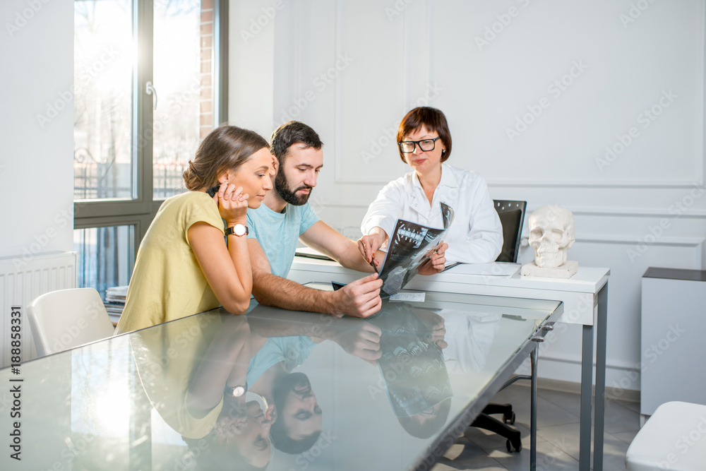 Young couple having a consultation with senior doctor discussing x-ray print sitting in the white of