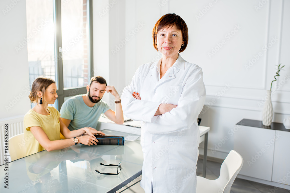 Portrait of a senior woman doctor standing with young couple of patients in the white office