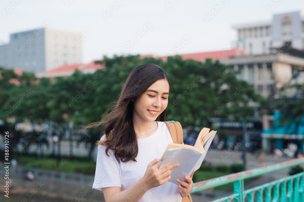 年轻漂亮的女孩在城市景观的桥上看书