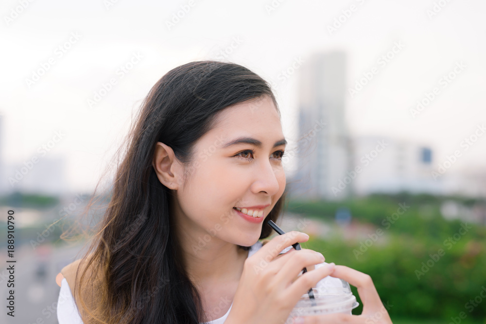 年轻漂亮的女孩站在桥上，手里拿着咖啡杯，可以看到城市的景色。