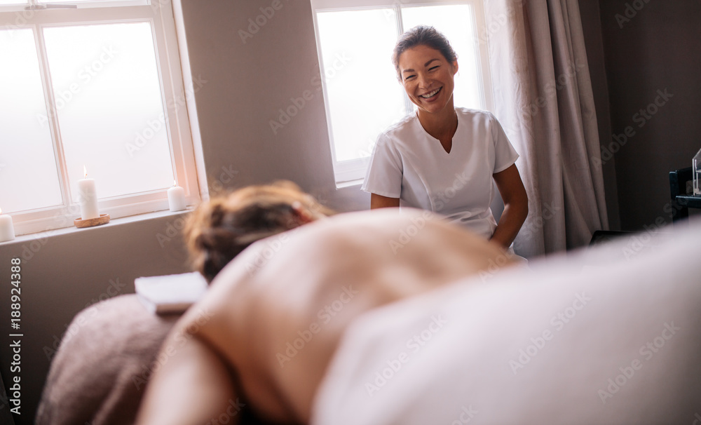 Masseur talking with female lying on massage table in spa salon