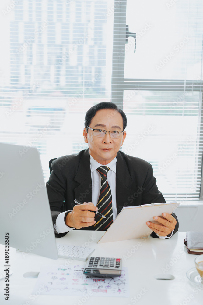 Senior financial asian businessman sitting at his workstation in front of computer.