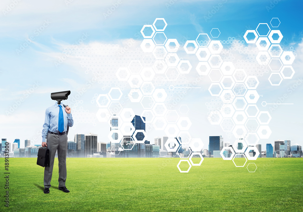 Camera headed man standing on green grass against modern cityscape