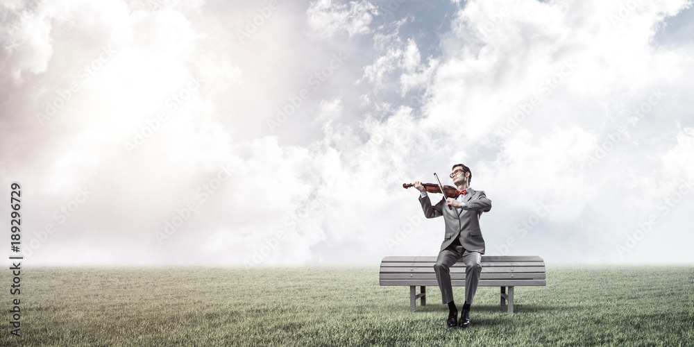 Handsome businessman in park on wooden bench play his melody