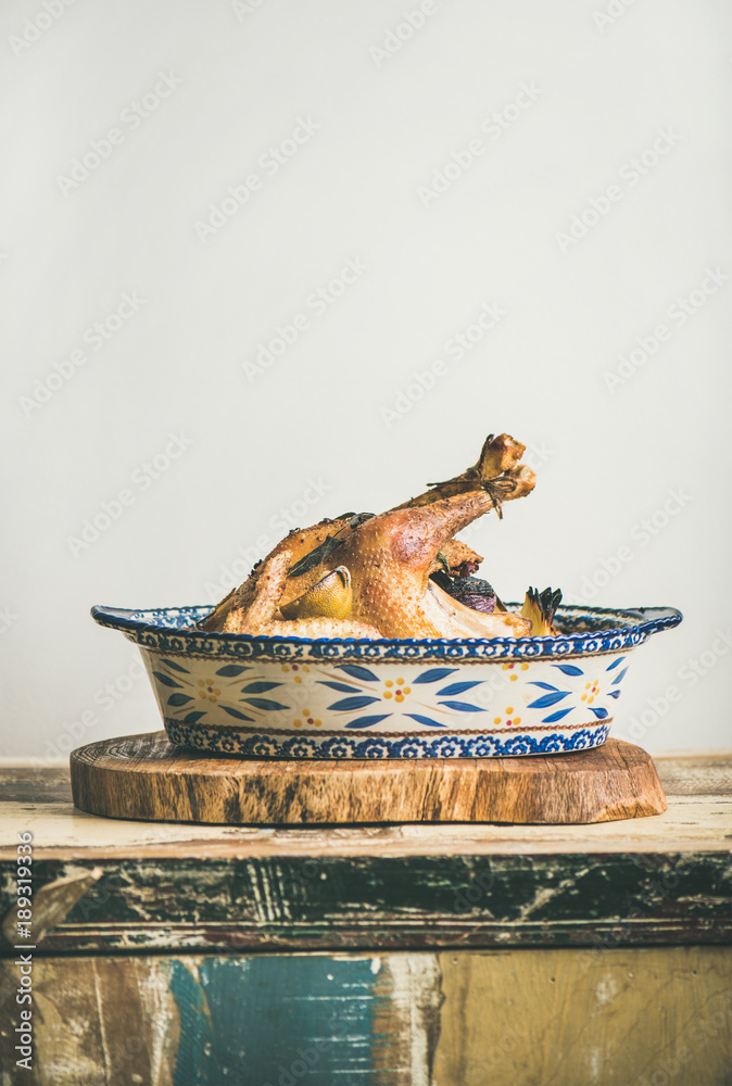 Roasted whole chicken for Christmas eve celebration table on rustic wooden board, light grey wall ba