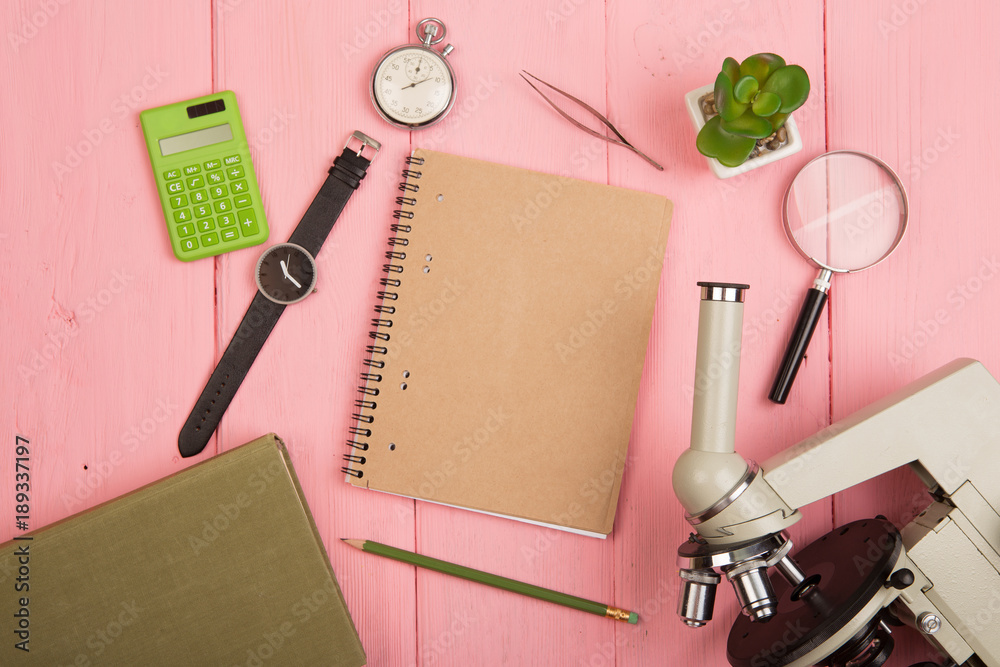 Education concept - notepad, microscope on the pink wooden desk