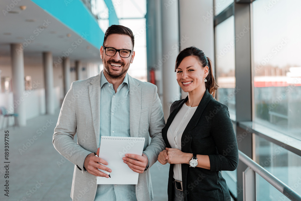 Portrait of two business people standing in office lobby.