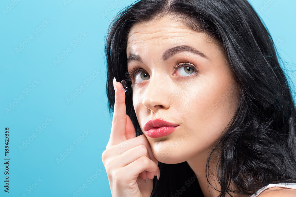 Beautiful young woman with contact lens on a solid background