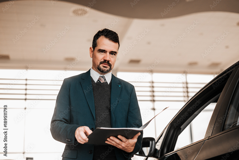 Portrait of a handsome car salesman in formalwear holding a clipboard.