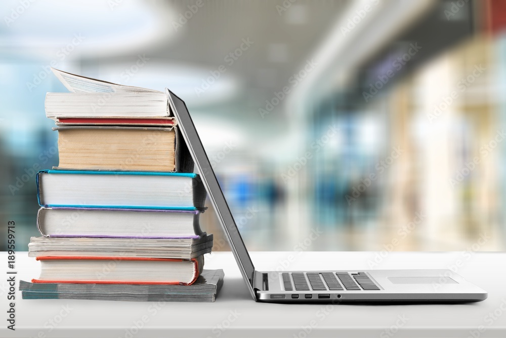 Stack of books with laptop on wooden table