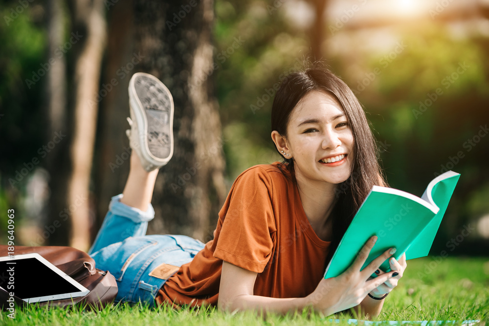 一个年轻或十几岁的亚洲女学生在大学里微笑着看书，看着平板电脑