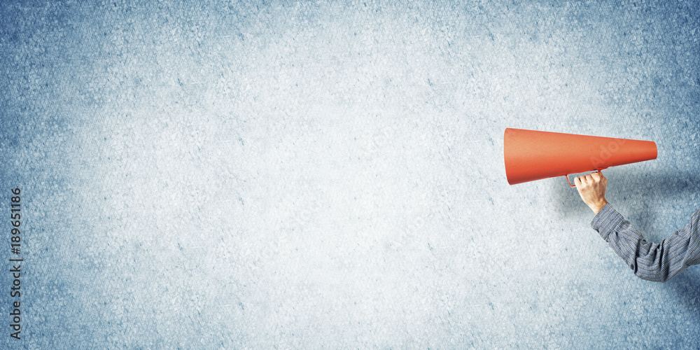 Hand of man holding paper trumpet against concrete background