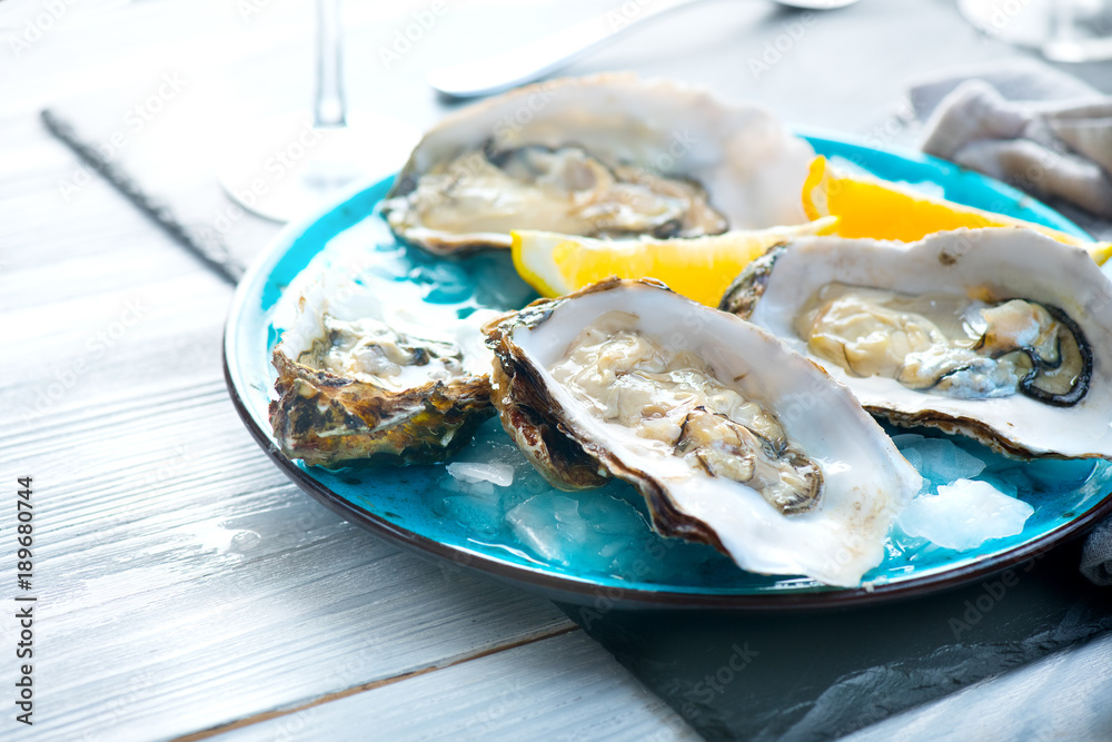 Fresh oysters close-up on blue plate, served table with oysters, lemon and champagne in restaurant. 