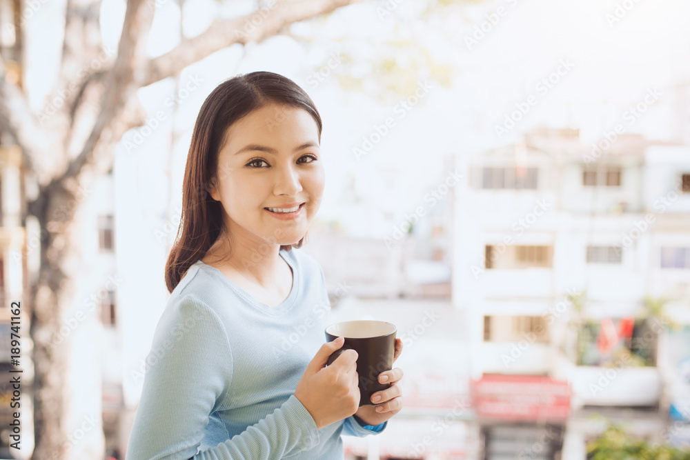 一个快乐的亚洲女人在早餐时拿着咖啡或茶杯思考的画像