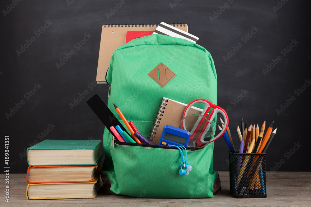 Education concept - school backpack with books and other supplies, blackboard background