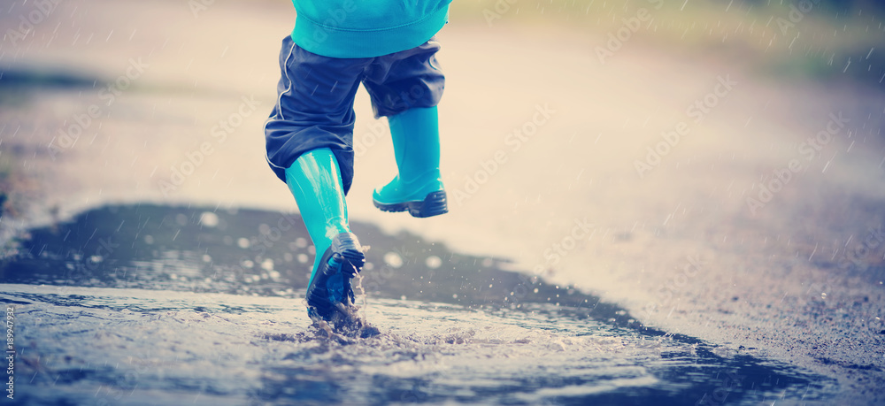 雨天孩子穿着雨鞋在水坑里行走