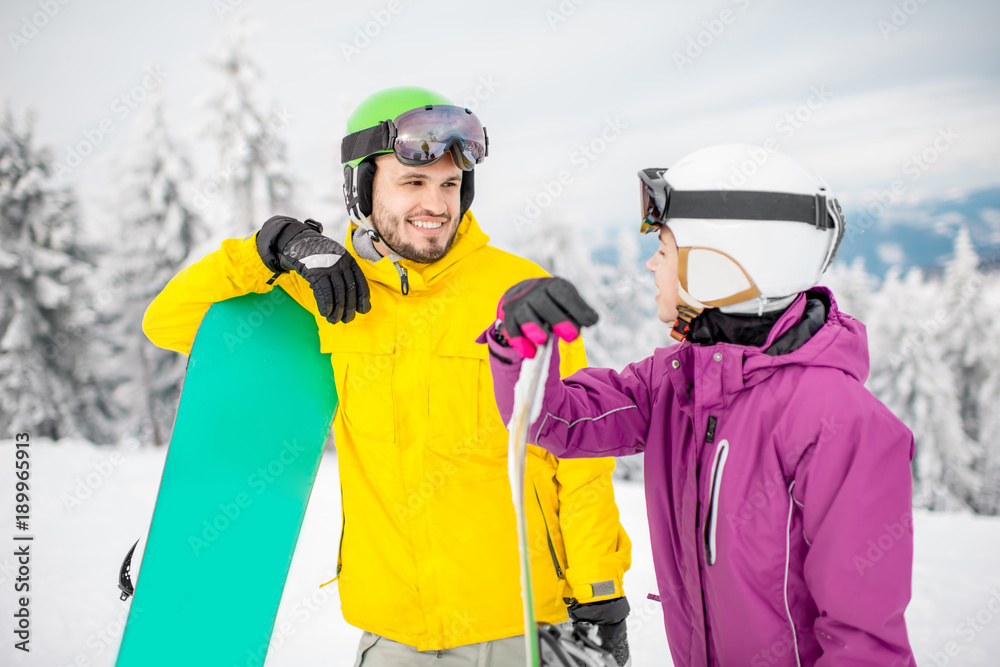 一对穿着冬季运动服的年轻情侣在冬季与滑雪板站在一起聊天