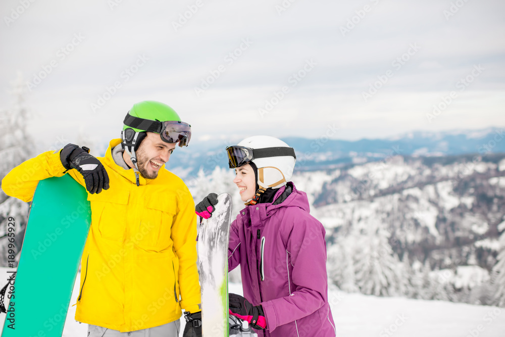 Young couple in winter sports clothes talking together standing with snowboards during the winter va