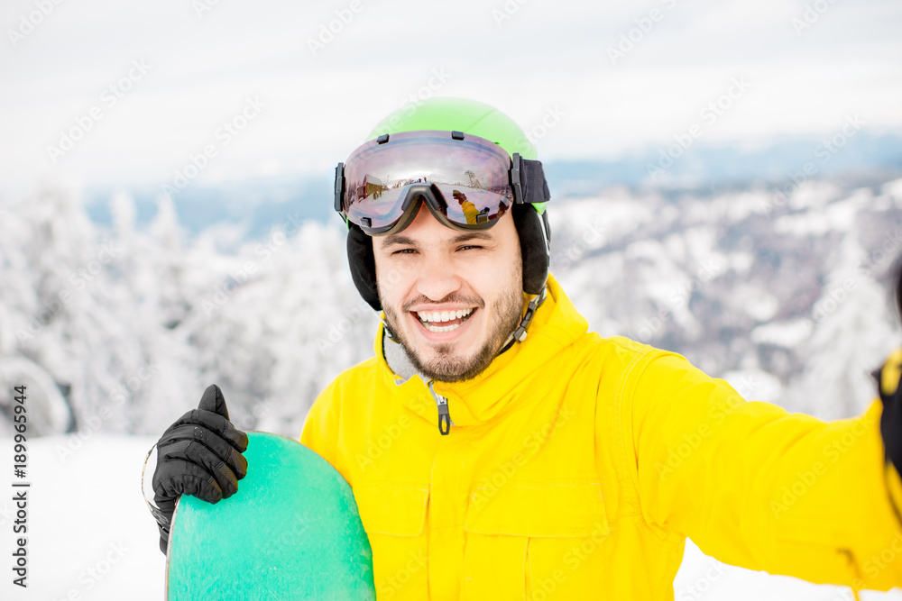 穿着冬季运动服的男子与滑雪板站在山上自拍