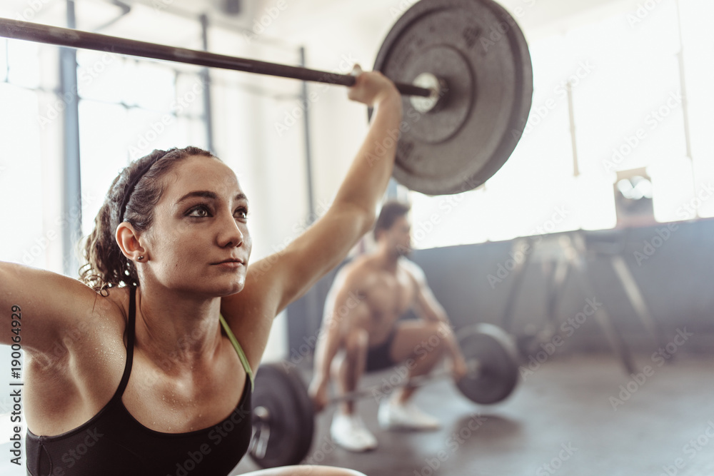 Tough young woman exercising with barbell