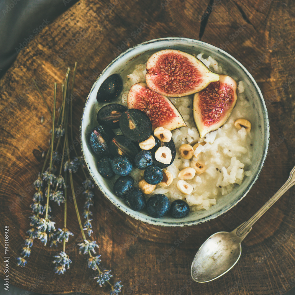 Healthy winter breakfast. Rice coconut porridge with figs, berries and hazelnuts in bowl over rustic