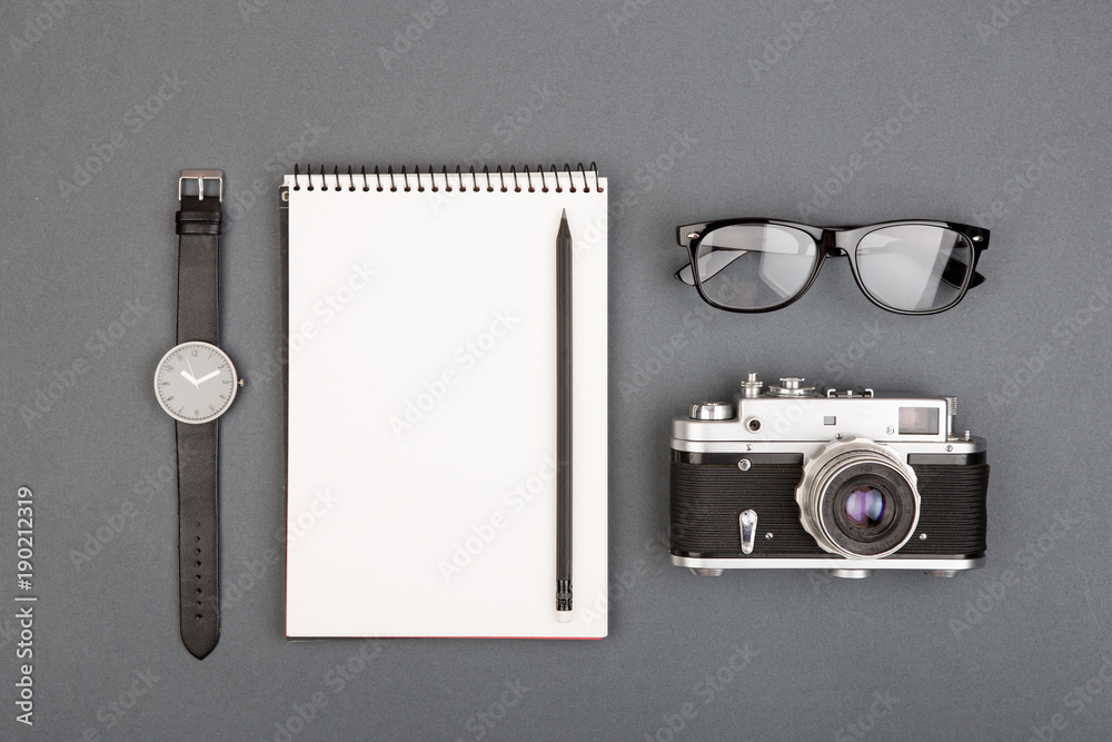 Journalist or blogger table - spiral blank notebook, pencil, camera and glasses on gray background, 