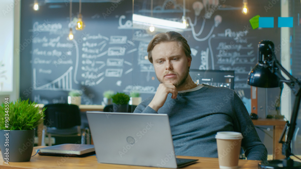 Handsome Young Office Employee Thinks on a Problem Solution While Working on a Laptop Computer. Hes