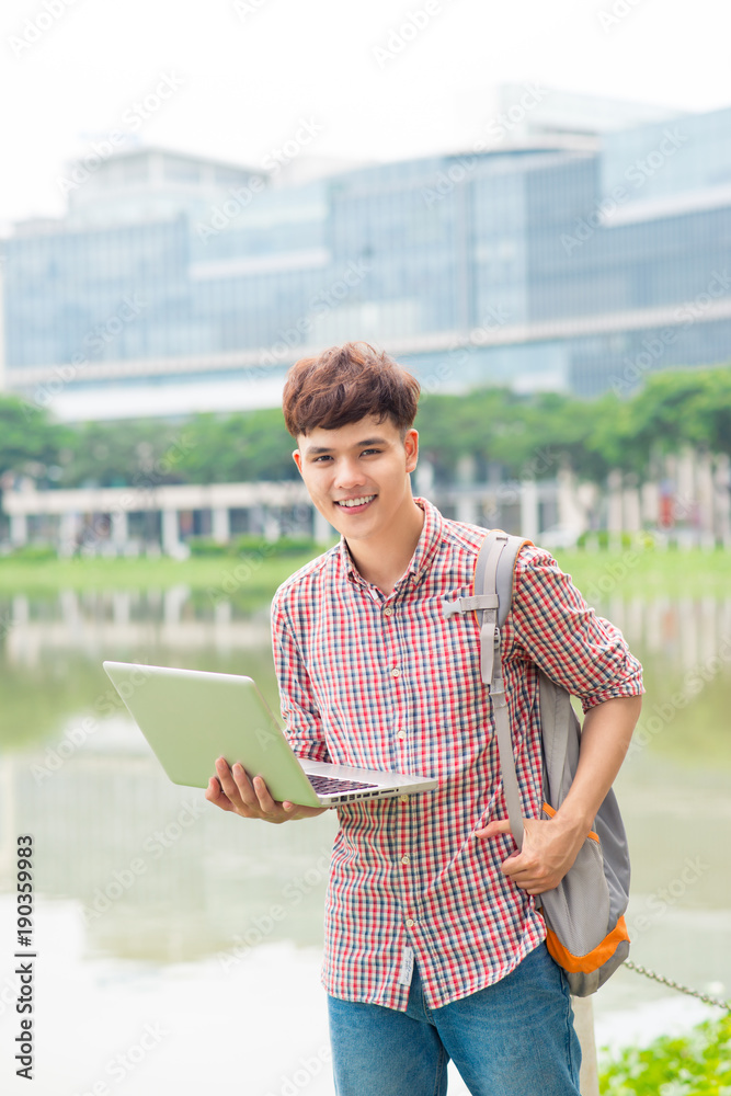 有魅力的亚洲男学生在校园里使用笔记本电脑