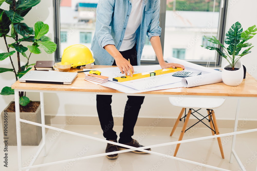 Engineer or architect in blue pullover is working on construction plans.